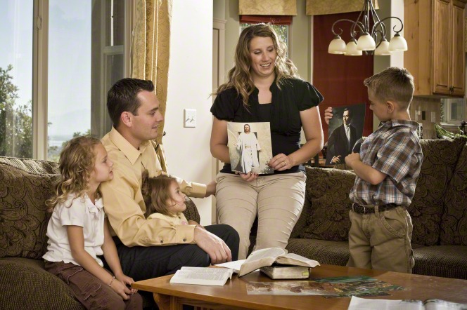 A mother and her son hold pictures of Jesus Christ and Joseph Smith while teaching a family home evening lesson to the rest of the family.