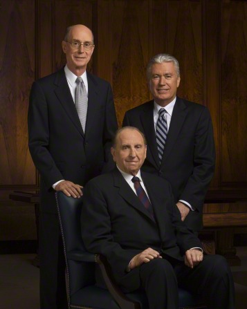 A portrait of the First Presidency, with President Monson in a chair, President Eyring standing behind him, and President Uchtdorf seated on a bench.
