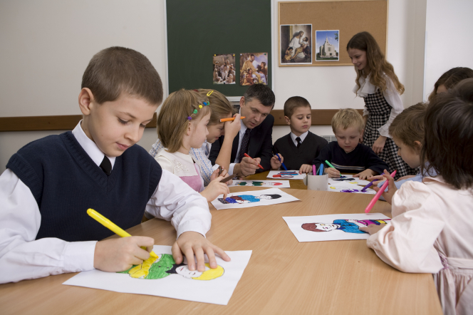 Four young boys and five young girls sit around a table and color a picture during a Primary class with the teacher at the head of the table.