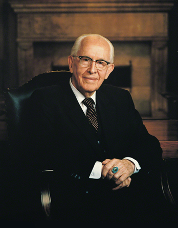 A portrait photograph by Busath Photography of Ezra Taft Benson in a dark suit and striped tie, sitting in a dark leather chair.