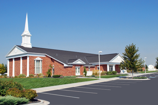 A side view of a parking lot and a red-brick chapel with a white steeple and a clear blue sky overhead in Caldwell, Idaho.