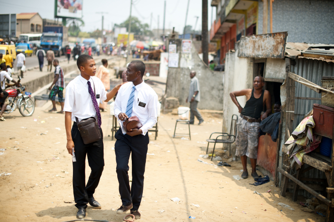 An elder missionary turning and putting his hand on his companion’s shoulder while talking and walking down a dirt street in Africa.
