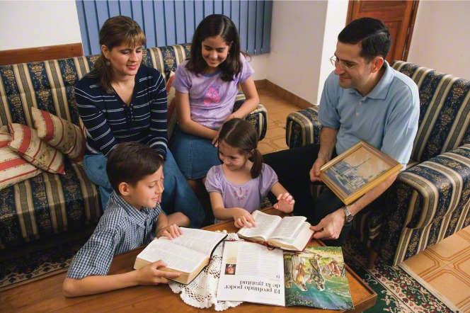 A family sitting in a living room with a Church magazine and the scriptures open for family home evening.