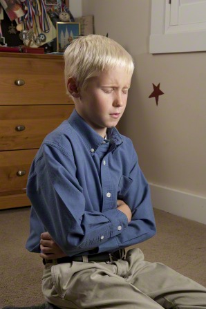 A young boy kneels down, folds his arms, and closes his eyes while saying a prayer in his bedroom.
