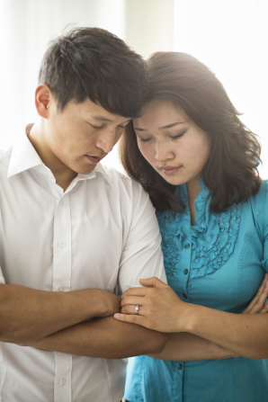 A young couple fold their arms and lean their heads together while they pray.