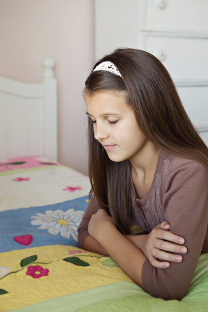 A young girl folds her arms and leans on her bed while she closes her eyes and prays.