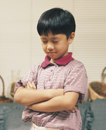 A young boy folds his arms, bows his head, and prays.