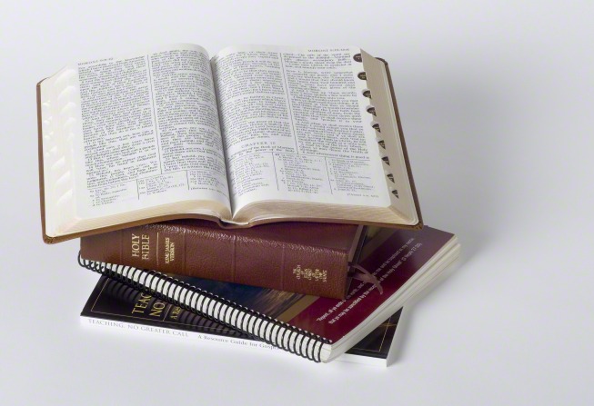 A brown triple combination resting on a stack of other books and lying open to Moroni chapter 9.
