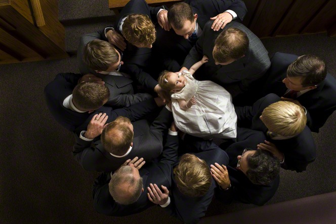 Eleven priesthood holders stand in a circle with a baby girl in their arms, giving her a blessing.