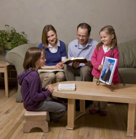 A family of four sitting together, looking at a painting of Joseph Smith from the Gospel Art Book.