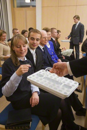 A woman with blond hair reaches out and takes a cup from a sacrament tray held out in front of her.