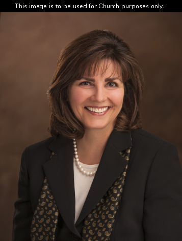 A portrait of Sister Carole M. Stephens, who is wearing a dark jacket and a patterned scarf, in front of a brown background.