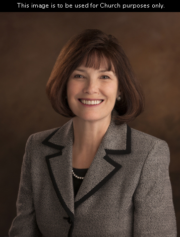 A portrait of Sister Linda S. Reeves, who is wearing a black and white jacket, in front of a brown background.