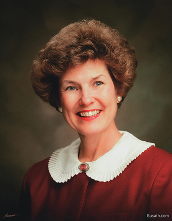 A photograph of Barbara Woodhead Winder against a gray background, wearing a red dress with a white collar.