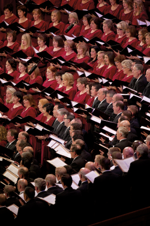 Rows of women in red dresses and men in black suits singing together in the Conference Center.