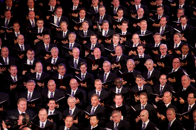 A section of the men from the Mormon Tabernacle Choir in black suits and purple ties, singing from the music they hold in their hands.