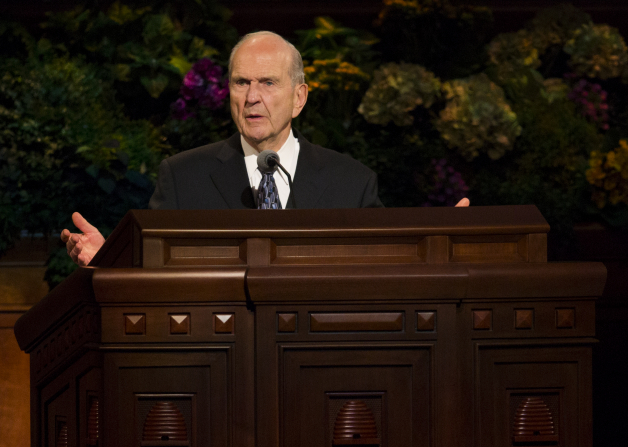 Russell M. Nelson standing with arms and hands slightly outstretched as he speaks behind the pulpit in general conference.