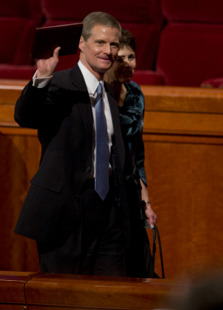 David A. Bednar waving with a journal in his hand as he and his wife exit the Conference Center.