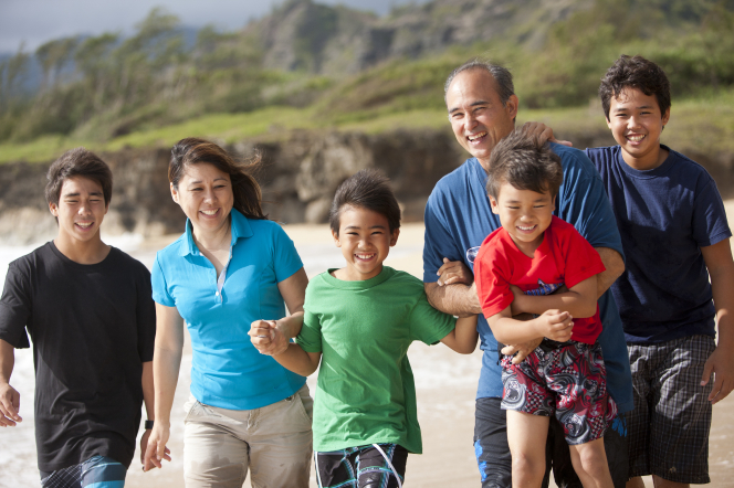 Two parents with their four sons walk on the beach.