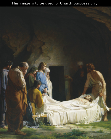 Christ’s friends wrapping His body in white linens to prepare Him to be placed into a tomb, which is seen in the background.