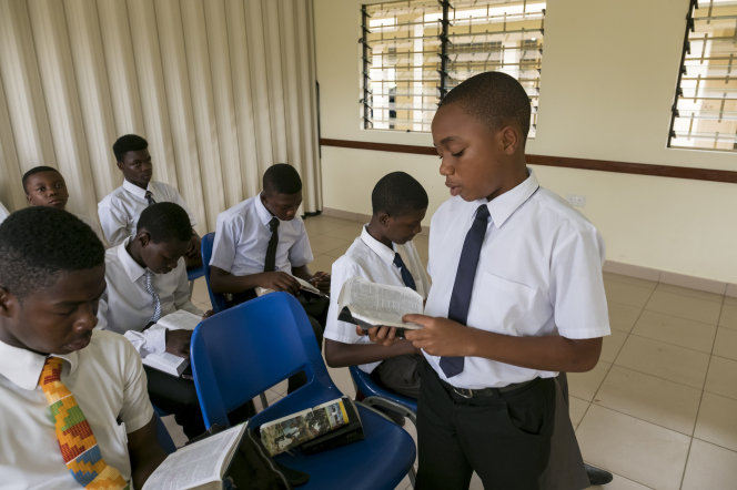 A group of young men sitting in a priesthood class in Ghana. One young man is standing and reading from the scriptures.