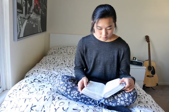 A young woman studies her scriptures on her bed.