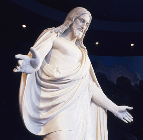 A white statue of Jesus Christ with arms outstretched, surrounded by a mural of blue sky.