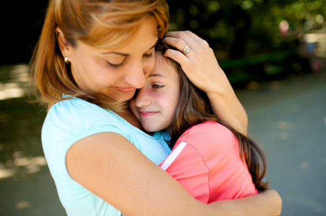 A red-haired woman pauses in the road to hug her daughter, who has dark hair and is wearing a pink jacket.