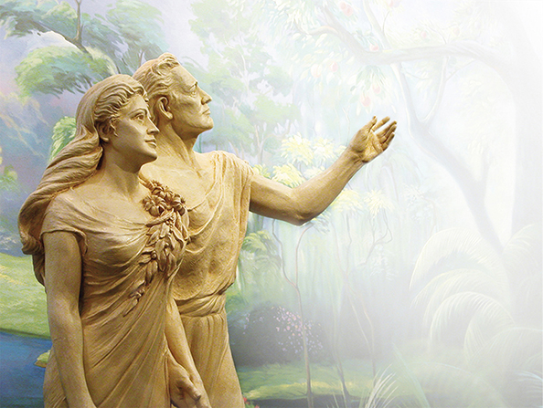 A statue of Adam and Eve standing together, with Adam reaching toward a tree shown in a mural.