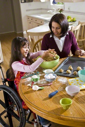 A mother and daughter sit at a table together and make cookies.