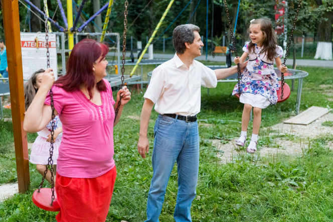 A mother and father in Moldova play on a swing set together with their two daughters.