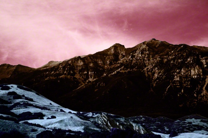 A pink sky hangs over a valley and a rocky mountain range.