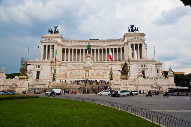 A lawn, vehicles, and people outside the Victor Emmanuel monument in Rome, Italy.