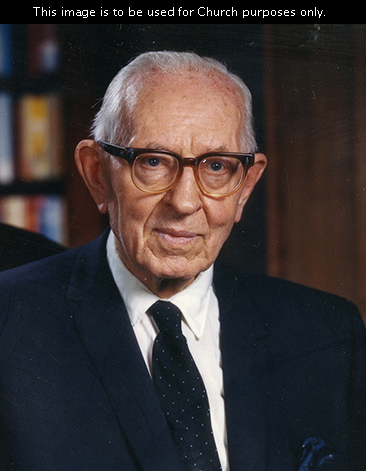 President Joseph Fielding Smith sitting in his office, wearing a white shirt, a dark suit, a dotted tie, and glasses.