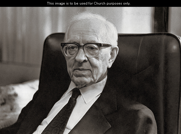 President Joseph Fielding Smith wearing a white shirt, a tie, a suit, and glasses, sitting in a black chair.
