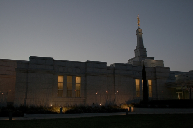 A view of the Adelaide Australia Temple at dusk, with the lights on the exterior walls and spire.