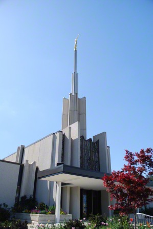 The front of the Atlanta Georgia Temple during the day, with a blue sky and a red tree on the grounds.