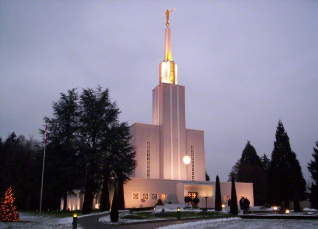 The Bern Switzerland Temple on a snowy evening, with a tree on the grounds strung with lit Christmas lights.