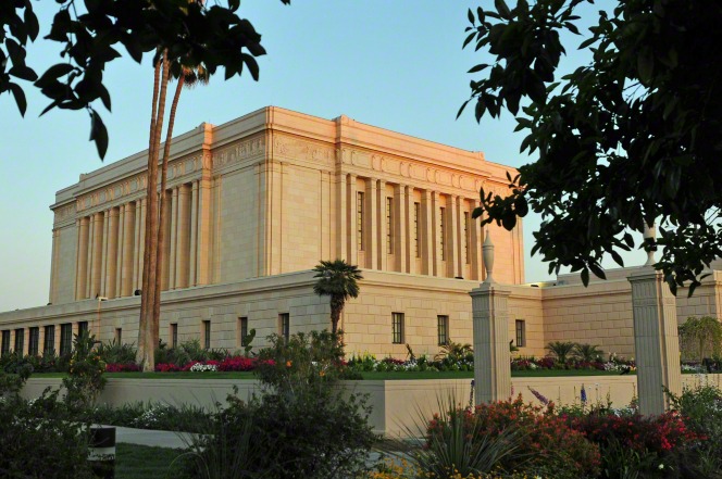 The Mesa Arizona Temple is viewed at an angle, with a landscape of grass and flowers and trees at sunset.