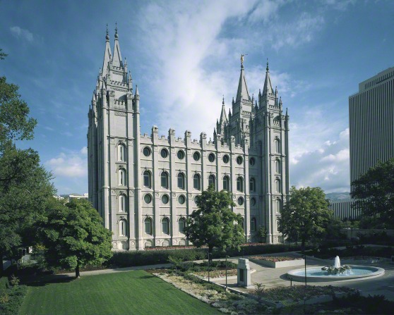 A side view of the entire Salt Lake Temple, with a view of the grounds around the temple, including a fountain and trees.